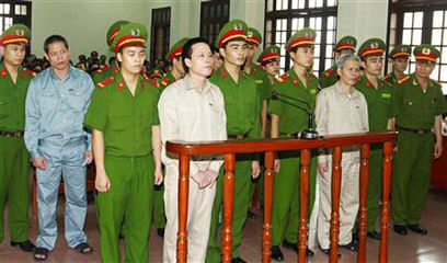 Doan Van Vuon (standing, 4th L), Doan Van Quy (standing, 2nd L) and Doan Van Sinh (standing, 3rd R) stand with policemen in front of the dock at a court during a verdict session in Hai Phong, 100 kilometres east of Hanoi, April 5, 2013, in this picture provided by the Vietnam News Agency. Photo: Reuters