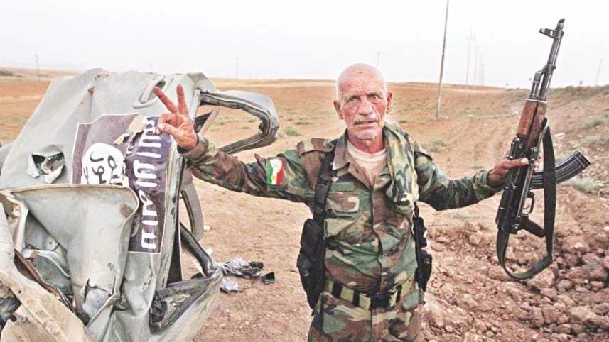 A Kurdish fighter poses next to a destroyed ISIS truck.
