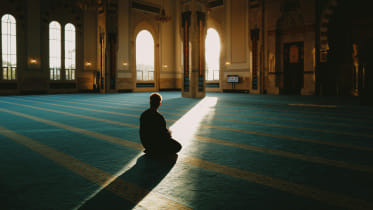 Person praying in a mosque with a sliver of sunlight pouring in.