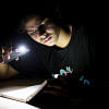 A photo of a boy studying with his phone's flashlight A photo of a boy studying with his phone's flashlight