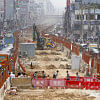 People crossing the street through the construction site of the metro railway.