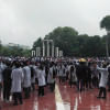 A large group of students who are wearing lab coats and standing in front of the Shaheed Minar