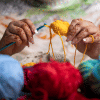 Artist crocheting with a yellow thread while three other shades of yarn are laid out in front of them.  Artist crocheting with a yellow thread while three other shades of yarn are laid out in front of them.