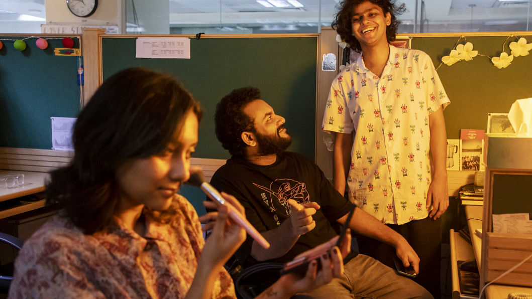 Male employees laughing at their female coworker who can be seen putting some makeup on.