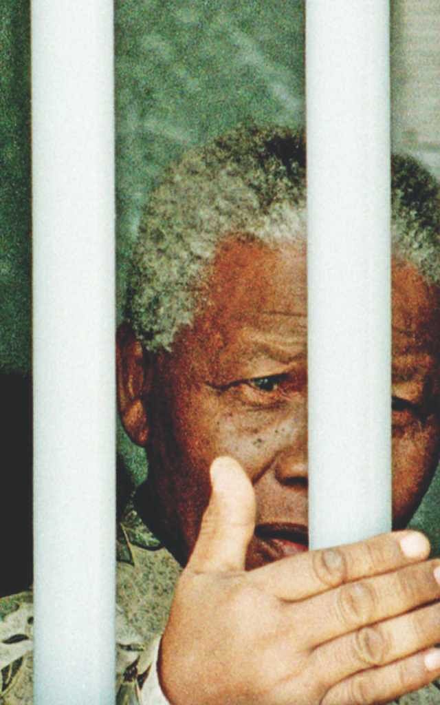 Nelson Mandela stands behind the bars of the former cell where he spent 18 of his 27 years as a political prisoner.