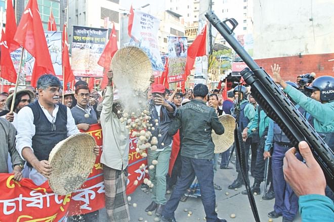 A farmer dumps his potatoes on the street in protest against the falling prices of the produce while policemen stand guard, in front of the National Press Club in Dhaka yesterday.  Photo: Star
