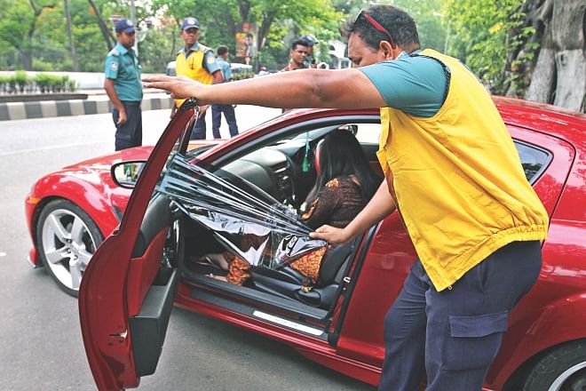 A policeman tears off the tinted sheet from the window of a sports car on Minto Road in the capital yesterday after the deadline for motorists to remove the tinted windows and screens from their vehicles ended on Saturday.  Photo: Amran Hossain