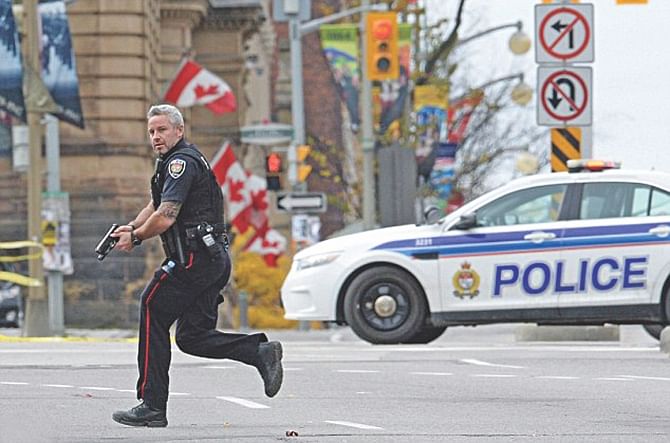 An police officer runs with his weapon drawn outside Parliament Hill in Ottawa yesterday after a gunman attacked the Parliament, injuring at least two people. Photo: AP, Reuters
