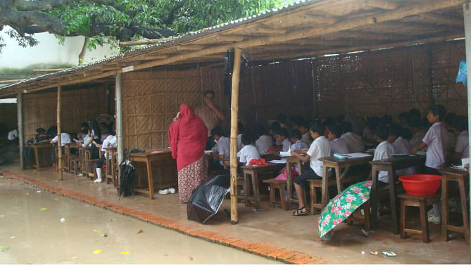 The kids of Model Government Primary School in Chapainawabganj town take classes in a make-shift shed during rain recently as the school building was declared risky and abandoned last year. PHOTO: STAR