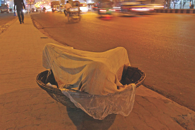 Cold bites :  Curled inside his basket he covered himself with his flimsy lungi to sleep on the median of Kazi Nazrul Islam Avenue near Karwan Bazar in the wee hours of yesterday as vehicles roll by on the street. The sudden drop in the mercury have put many in trouble, like this labourer in the photo.  Photo: Anisur Rahman