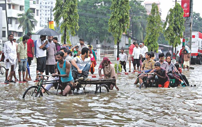 People try to get to work on rickshaw vans ploughing through over knee-deep water on a street in Muradnagar of Chittagong yesterday as overnight heavy showers that stopped around 10:00am inundate several areas of the port city.  Photo: Anurup Kanti Das