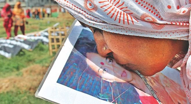 With all her love, Safura Khatun kisses the photo of her daughter Rashida, a Rana Plaza victim, near her grave at Jurain graveyard in the capital yesterday. She kept the photo with her for the last one year, looking for her child who was buried unidentified there before a DNA test confirmed her identity in February and paved the way for her family to know at least where she is laid to rest. Photo: Anisur Rahman