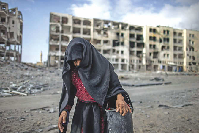 An elderly Palestinian woman carries a bucket as she walks past destroyed buildings in Beit Lahia in the northern Gaza Strip yesterday, with the Israeli-Hamas conflict entering its 27th day in the besieged territory.  Photo: AFP