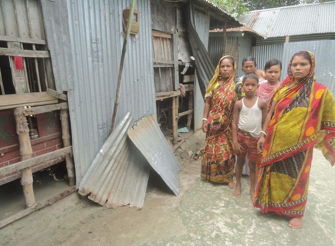 Members of a panic-stricken Hindu family stand in front of their house vandalised by a gang of extortionists at Nizpara village in Lalmonirhat Sadar upazila on Monday. Photo: Star