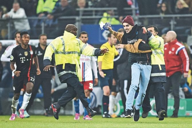 A Hamburg fan who ran on to the pitch and hit Bayern Munich midfielder Franck Ribery in the face with his scarf is tackled by security staff during the German Cup match in Hamburg on Wednesday.  Photo: AFP