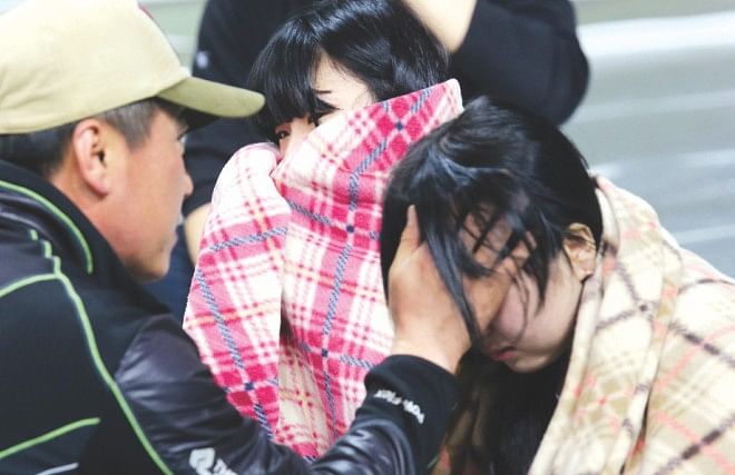 Survivours wrapped in blankets react as they are brought onto land. Photo: AFP