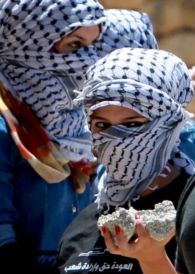 Palestinian women wearing traditional Keffiyeh head scarf gather stones to be thrown at an Israeli guard tower in the West bank city of Bethlehem during a protest. Photo: AFP