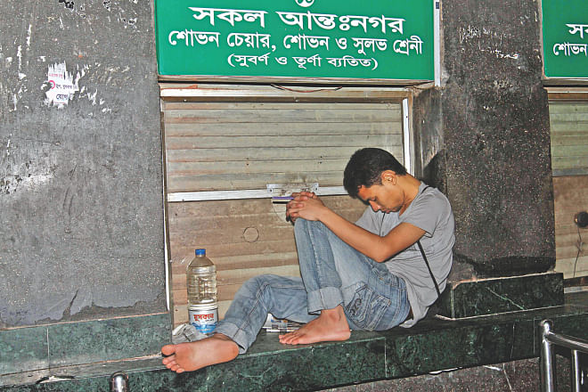 In an awkward position, a man sleeps on a ticket counter at Kamalapur Railway Station in the wee hours of yesterday to keep his first place in line for advance tickets for Eid. He had been waiting there since 5:00pm Saturday. He got the tickets around 9:00am yesterday. Photo: Anisur Rahman