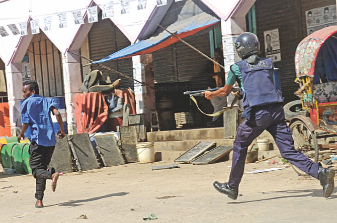A short gun-holding cop chases a man following a clash between transport workers and students in Sylhet's Mendibag area. The photo was taken yesterday.   Photo: Star