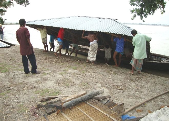 A flood-hit family of Char Dawabari in Hatibandha upazila of Lalmonirhat district puts the corrugated iron roof of their house onto a boat to take it to a safer place. Photo: Star