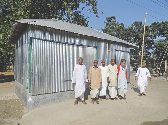  Some of the Hindus, affected during Jamaat-Shibir men's vandalism and looting on October 27 last year, pose in front of a repaired shop at Shafinagar village in Bawra union under Patgram upazila under Lalmonirhat district on Monday. Several other victims, however, are yet to repair their shops and houses, damaged during the attack, for want of money.    PHOTO: STAR