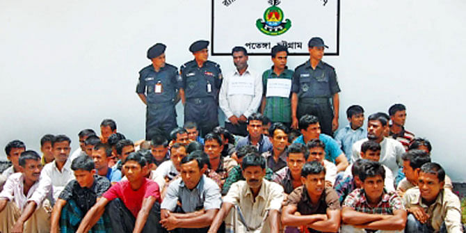 This July, 2012 photo shows 48 men rescued by Rapid Action Battalion while being trafficked to Malaysia through the Bay of Bengal and the two arrested traffickers, standing, in Chittagong.