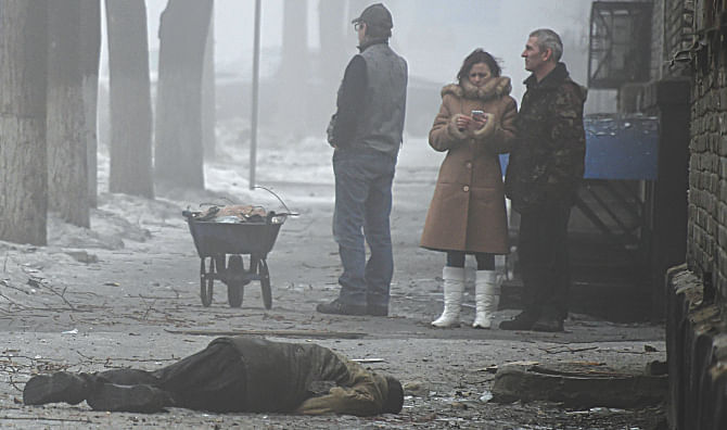 People stand beside the body of a man killed after a shell hit a residential area, killing two civilians in Donetsk's Kyibishevsky district on Friday.  Photo: AFP