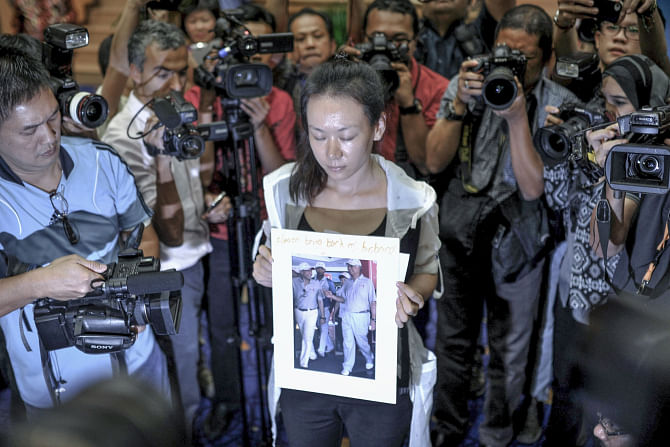 A relative (C) of a passenger of the missing Malaysia Airlines flight MH370 holds a picture of Malaysian Prime Minister Najib Razak with the writing ‘Please bring back my husband’ in Putrajaya, yesterday. Photo: AFP