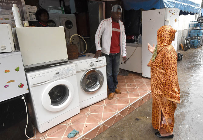 Centre, Ivorian migrant Moctar Toure talks to a Moroccan costumer in front of his household repairs shop in the Moroccan capital Rabat. Photo: AFP/File
