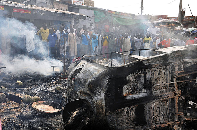 People gather to look at a burnt vehicle following a bomb explosion that rocked the busiest roundabout near the crowded Monday Market in Maiduguri, Borno State, on July 1, 2014. Photo: Getty Images