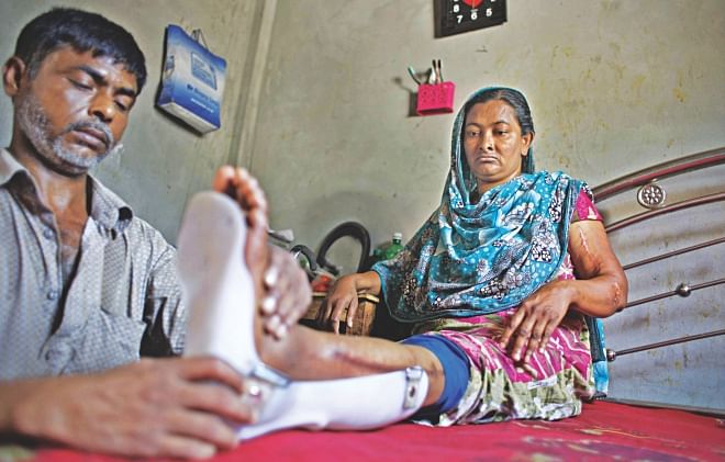Hasu attaches an ankle-foot orthosis to the left leg of his wife Feli, one of the workers pulled out alive from the rubble of Rana Plaza last year. With a paralysing feeling in her left leg and inability to bend her left arm, she is almost immobile and completely dependent on her husband. Hasu had to quit his job as a caretaker of a house nearby to take care of the family. The photo was taken yesterday.  Photo: Rashed Shumon
