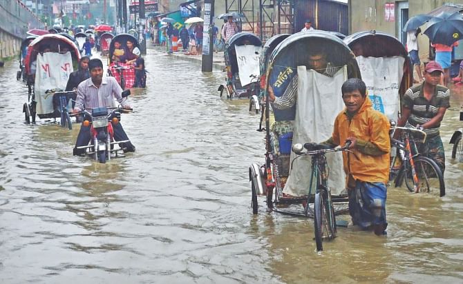 People head to work yesterday morning wading through knee-deep water on a street in Bahaddarhat.   Photo: Star