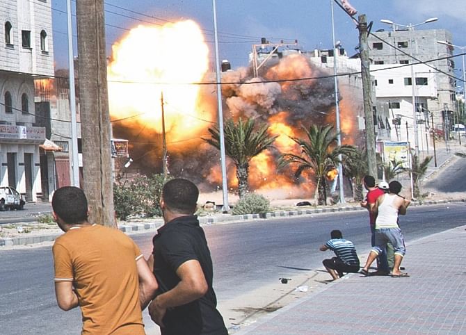 Palestinian men look on as a bomb from an Israeli air strike hits a house in Gaza City on August 23, 2014.  Photo: AFP