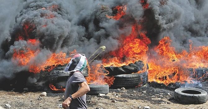 A Palestinian protester, near burning tyres, uses a slingshot to target Israeli security forces during clashes, against the expansion of Israeli settlements, in the village of Kfar Qaddum near the northern city of Nablus, in the occupied West Bank yesterday. Israel published tenders for 283 new homes in a West Bank settlement on October 5, just days after announcing its biggest land grab on occupied Palestinian territory for three decades. Photo: AFP