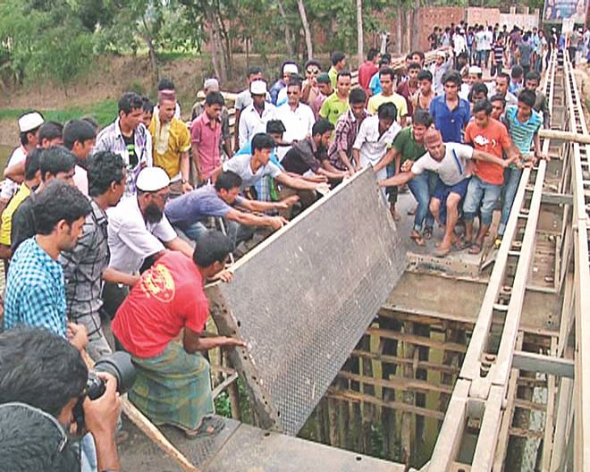 A group of Phulgazi residents protesting against the killing of the upazila chairman Ekramul Haque pull apart the metal planks of Feni-Parsuram bailey bridge in Bandua of the upazila, disrupting road communications there for about seven hours yesterday. Ekram, also an Awami League leader, was shot inside his SUV before being burnt alive by unidentified assailants in Feni town on Tuesday. Photo: Banglar Chokh