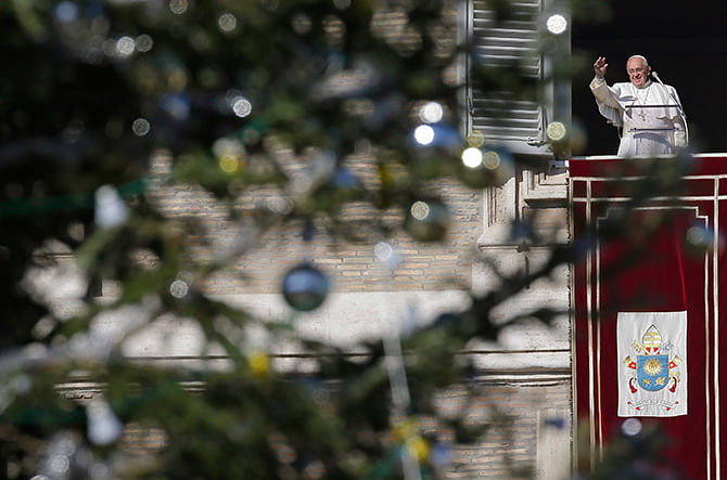 The Vatican Christmas tree frames Pope Francis as he waves to the faithful during the Angelus prayer in Saint Peter's Square at the Vatican December 21, 2014. Photo: Reuters