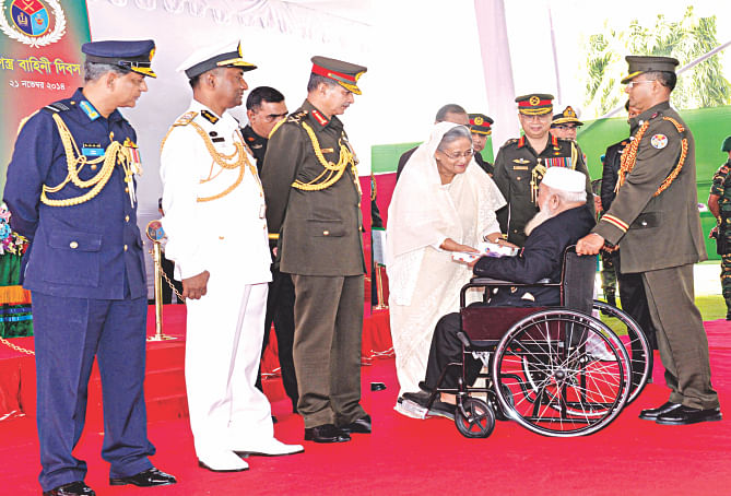 Prime Minister Sheikh Hasina hands over a gift to a decorated freedom fighter during the Armed Forces Day celebrations at Dhaka Cantonment yesterday while Chief of Army Staff General Iqbal Karim Bhuiyan, Chief of Navy Staff Vice Admiral Muhammad Farid Habib and Chief of Air Staff Air Marshal Muhammad Enamul Bari look on. Photo: PMO