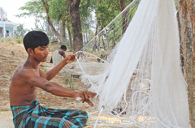 Fishermen, otherwise free due to the ongoing ban on catching jatka, pass their time weaving and mending their fishing nets. The photo was taken from Majhibari in Kuakata sea beach area of Patuakhali yesterday.  PHOTO: STAR