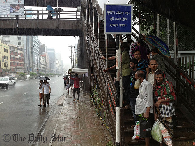 City dwellers take shelter under the shade of a foot-overbridge to dodge the heavy downpour that started from Wednesday evening. This STAR file photo was taken from capital's Kazi Narzul Islam Avenue.