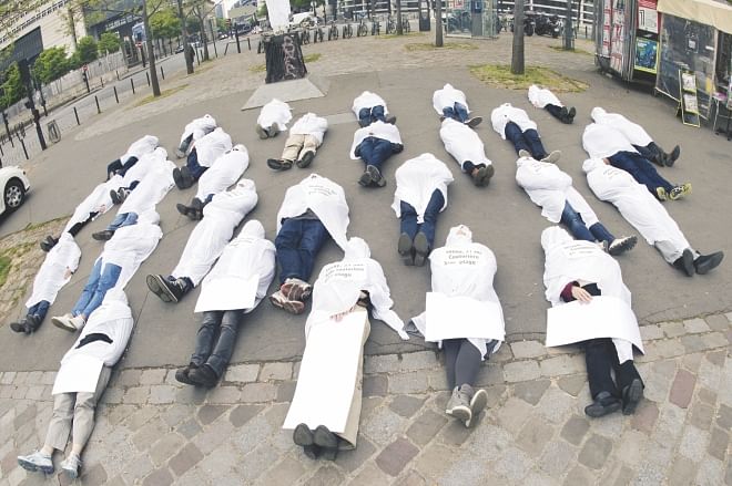 People wear funeral shrouds and lie on the ground in Paris yesterday as they take part in a protest marking the first anniversary of the Rana Plaza collapse in Bangladesh. Photo: AFP