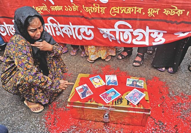 A sobbing Rokeya Begum sits before a trunk filled with fake money and covered with red paint symbolising the blood of missing workers of Tazreen Fashions whose photos are pasted on it during a human chain in front of Jatiya Press Club yesterday which demanded compensation from the prime minister's relief fund for the missing and the injured; her daughter Hena is one of the missing. Photo: Star