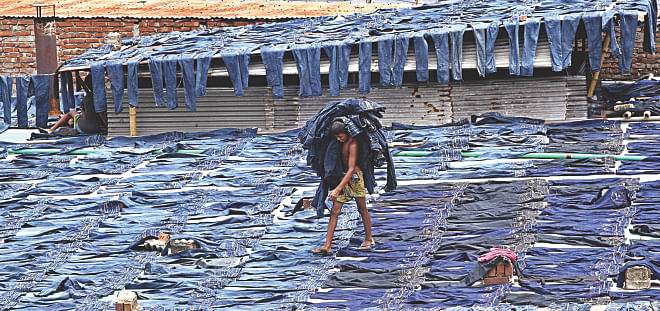 A worker collects pairs of dyed jeans from rooftops in the apparel hub of Keraniganj in Dhaka yesterday. Factories in the area produce denim and woven items and mostly target lower and middle income groups.  Photo: Amran Hossain 