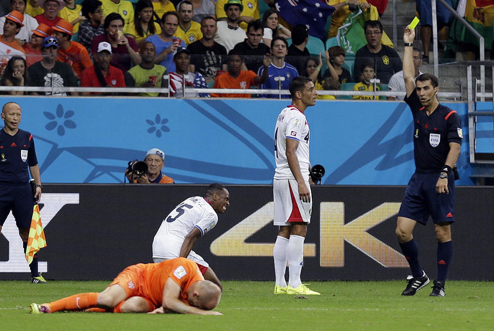Costa Rica's Michael Umana is booked with a yellow card by referee Ravshan Irmatov from Uzbekistan after an incident with Netherlands' Arjen Robben, left, during the World Cup quarterfinal soccer match at the Arena Fonte Nova in Salvador, Brazil, Saturday, July 5, 2014.