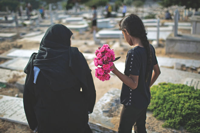 A Palestinian woman and a girl carry flowers to a family grave on Eid at a cemetery in Gaza City on Monday. Photo: Reuters 