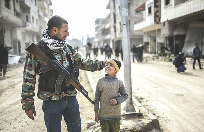 A Kurdish fighter walks with his child in the center of the Syrian border town of Kobane, yesterday. Photo: AFP