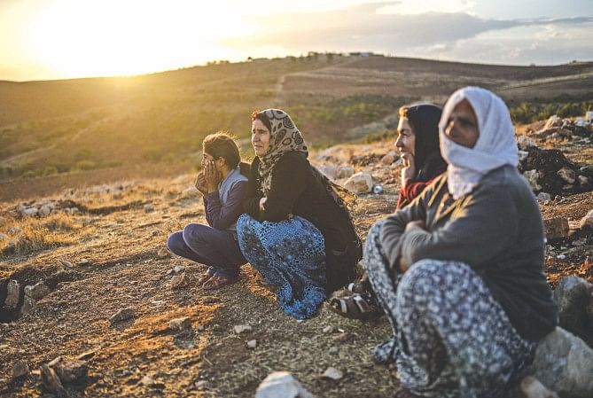 Syrian Kurds, facing genocide, sit on a hill looking down on clashes between jihadists of the ISIS and Kurdish fighters, close to the Turkish-Syrian border in Sanlinurfa province.   Photo:  AFP