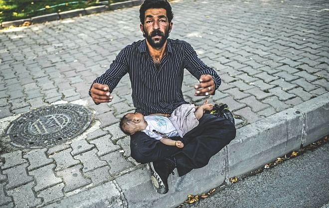 Refugee Crisis: A Syrian refugee man gestures as he begs in the street with a baby lying on his lap in Istanbul on Thursday. Nearly half of Syria's population has fled their homes since the uprising against President Bashar al-Assad's rule erupted in March 2011. The UNHCR said there were 51.2 million forcibly displaced people at the end of 2013, a full six million higher than the previous year.  Photo: AFP