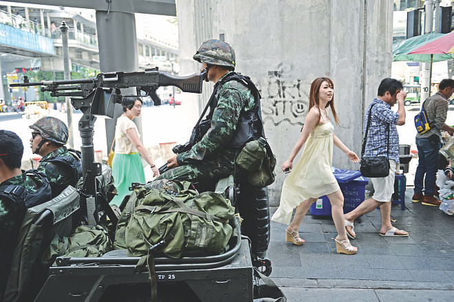 People walk past Thai army soldiers sitting in a jeep mounted with a machine gun as they secure a main intersection in Bangkok, yesterday. Thailand's army declared martial law across the deeply divided kingdom yesterday to restore order after months of deadly anti-government protests, deploying armed troops in the capital but insisting the move was 