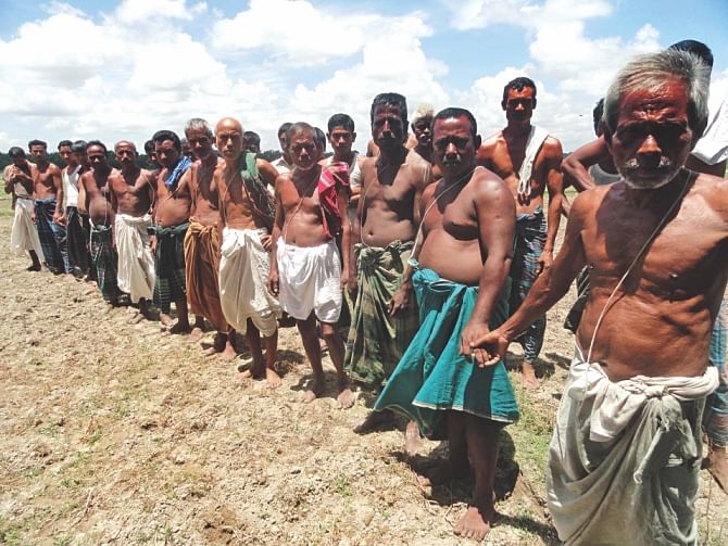 The Hindu farmers, who own most of the 800-bigha beel but are barred from using the part where the pisciculture is going on, form a human chain near their fields yesterday. Although the upazila nirbahi officer ordered the BNP men to remove the fence by July 25, they seem not to care at all. Photo: Star