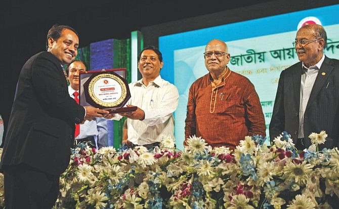 Finance Minister AMA Muhith presents crests to top taxpayers at a ceremony organised by the National Board of Revenue at Sonargaon Hotel in Dhaka yesterday. Ghulam Hussain, chairman of NBR, and Kazi Akram Uddin Ahmed, president of the Federation of Bangladesh Chambers of Commerce and Industry, were also present.  Photo: Star 